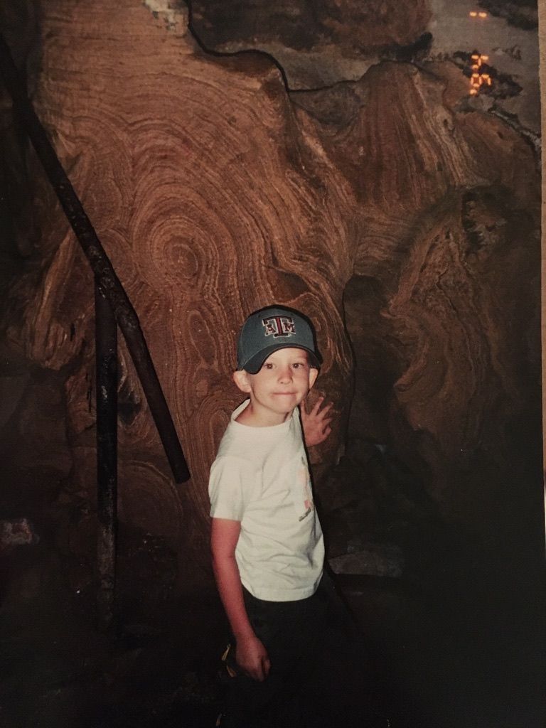 Miguel as a child in a Texas A&M cap, standing in front of folded rock strata